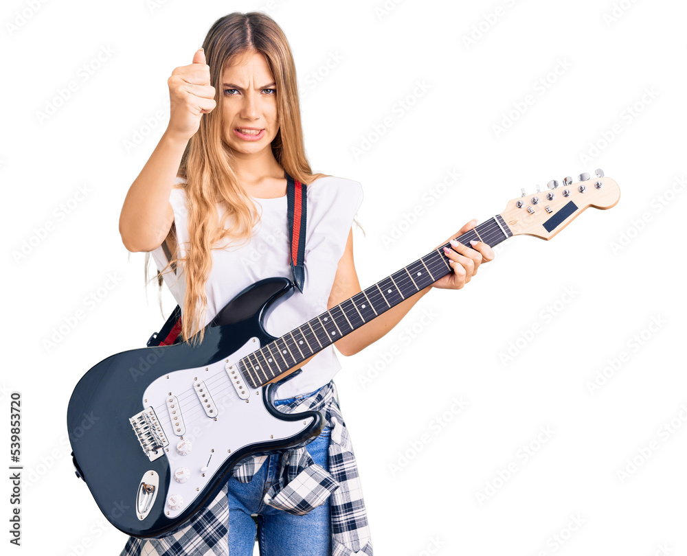 Beautiful caucasian woman with blonde hair playing electric guitar annoyed and frustrated shouting with anger, yelling crazy with anger and hand raised