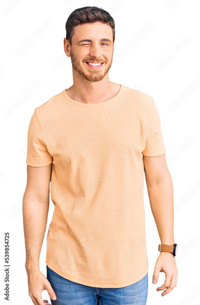 Fototapeta premium Handsome young man with bear wearing casual yellow tshirt winking looking at the camera with sexy expression, cheerful and happy face.