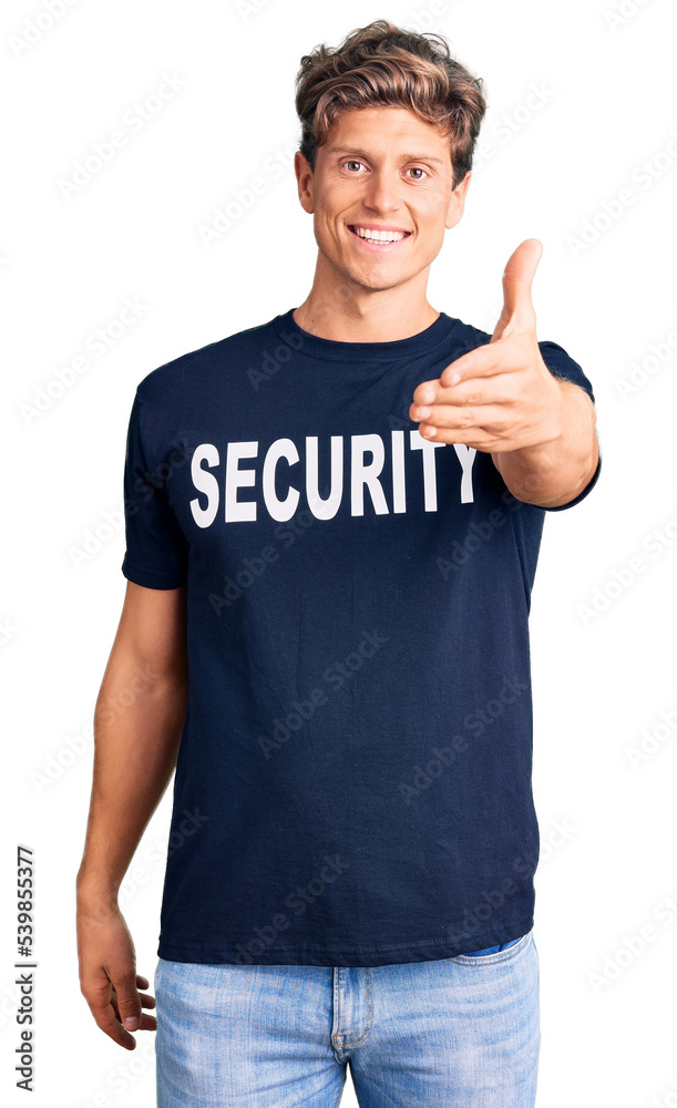 Young handsome man wearing security t shirt smiling friendly offering handshake as greeting and welcoming. successful business.