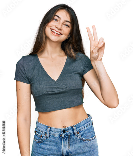 Young beautiful teen girl wearing casual crop top t shirt showing and pointing up with fingers number two while smiling confident and happy.