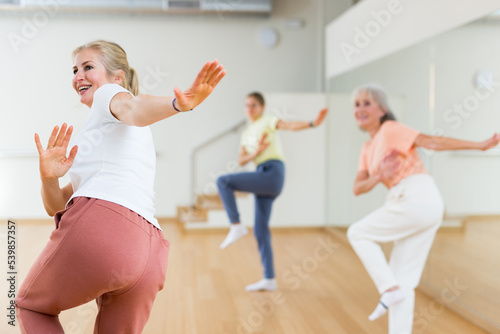 Portrait of cheerful active blonde female exercising dance moves in fitness studio