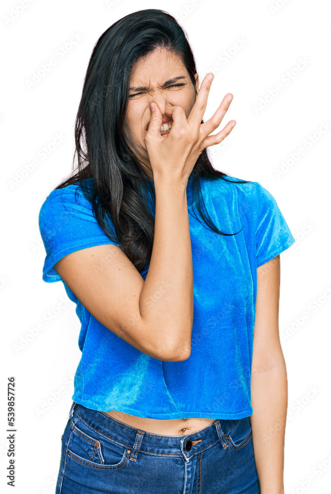 Young hispanic woman wearing casual clothes smelling something stinky and disgusting, intolerable smell, holding breath with fingers on nose. bad smell Young hispanic woman wearing casual clothes smelling something stinky and disgusting, intolerable smell, holding breath with fingers on nose. bad smell