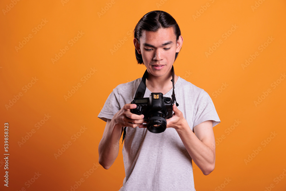 Young photographer taking photos on professional dslr camera, looking at electronics display. Attractive asian man photographing, front view medium shot, creative hobby, photoshoot Young photographer taking photos on professional dslr camera, looking at electronics display. Attractive asian man photographing, front view medium shot, creative hobby, photoshoot