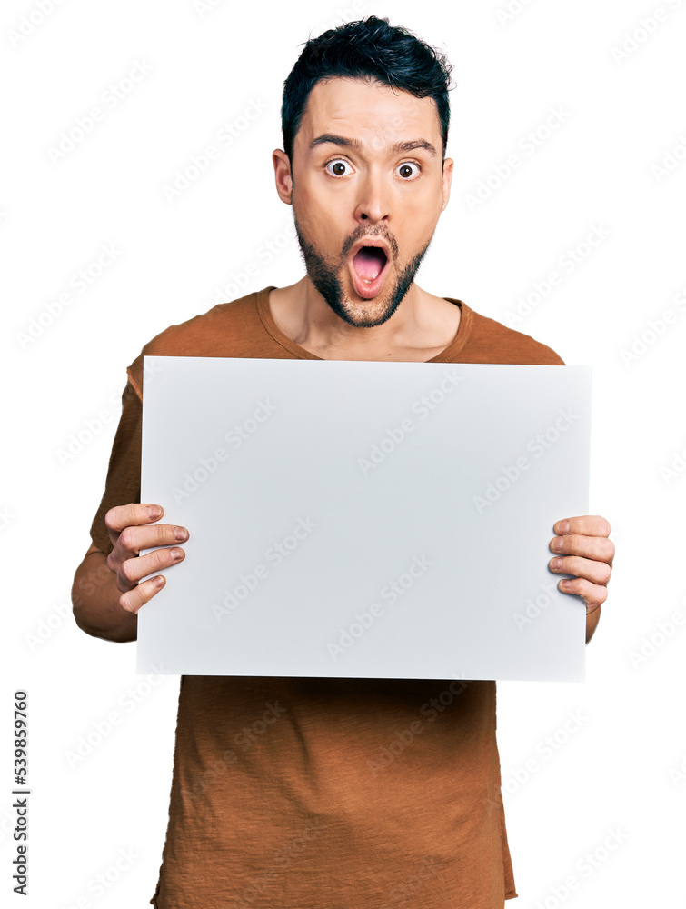 Hispanic man with beard holding blank empty banner afraid and shocked with surprise and amazed expression, fear and excited face. Hispanic man with beard holding blank empty banner afraid and shocked with surprise and amazed expression, fear and excited face.