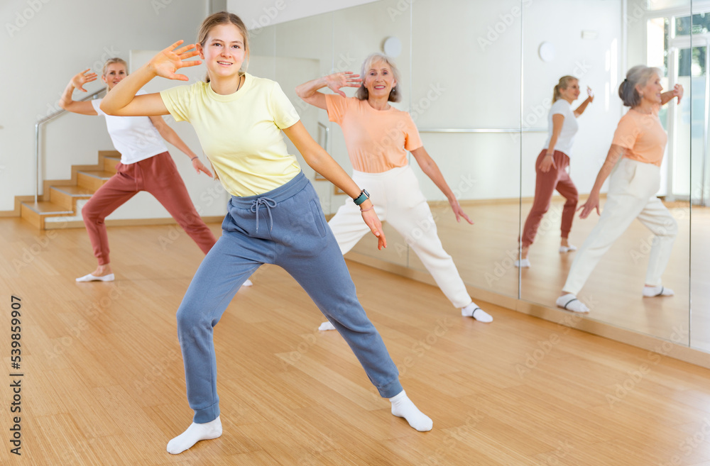 Positive teen girl with family doing aerobics exercises with group of people in dance center
