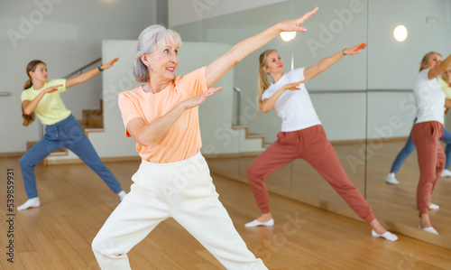 Mature adult female dancing with other women during group class in dance center