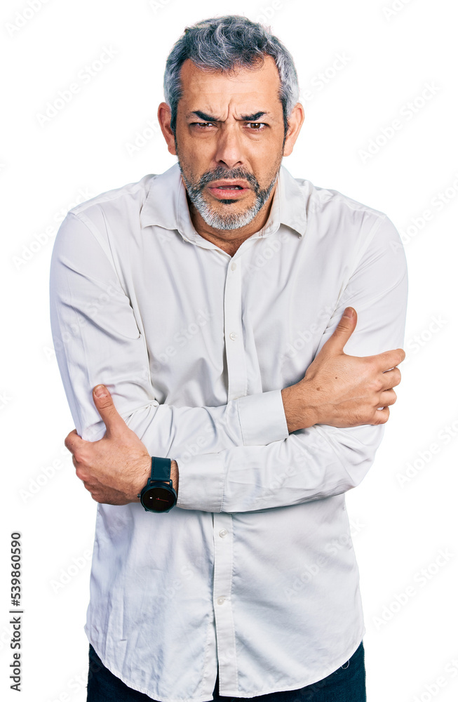 Middle age hispanic with grey hair wearing casual white shirt shaking and freezing for winter cold with sad and shock expression on face Middle age hispanic with grey hair wearing casual white shirt shaking and freezing for winter cold with sad and shock expression on face