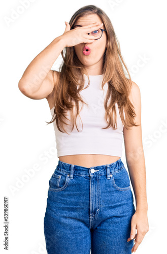 Beautiful caucasian young woman wearing casual clothes and glasses peeking in shock covering face and eyes with hand, looking through fingers with embarrassed expression. © Krakenimages.com
