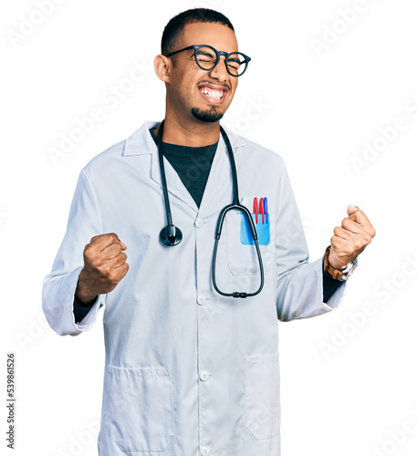 Young african american man wearing doctor uniform and stethoscope very happy and excited doing winner gesture with arms raised, smiling and screaming for success. celebration concept. © Krakenimages.com