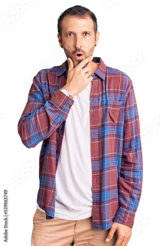 Young handsome man wearing casual clothes looking fascinated with disbelief, surprise and amazed expression with hands on chin
