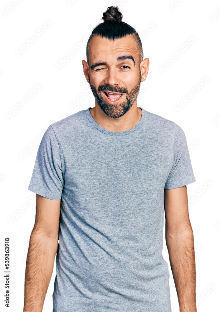 Hispanic man with ponytail wearing casual grey t shirt winking looking at the camera with sexy expression, cheerful and happy face. Hispanic man with ponytail wearing casual grey t shirt winking looking at the camera with sexy expression, cheerful and happy face.
