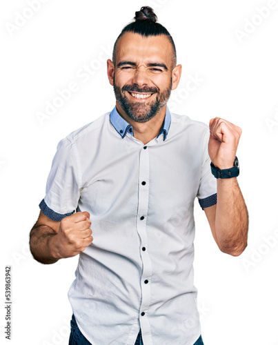 Hispanic man with ponytail wearing casual white shirt celebrating surprised and amazed for success with arms raised and eyes closed. winner concept.