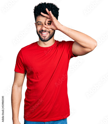 Young arab man with beard wearing casual red t shirt doing ok gesture with hand smiling, eye looking through fingers with happy face.