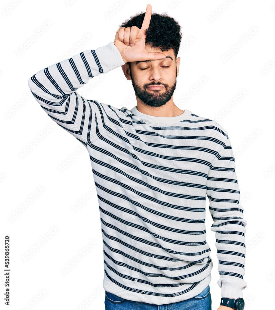 Young arab man with beard wearing casual striped sweater making fun of people with fingers on forehead doing loser gesture mocking and insulting. Young arab man with beard wearing casual striped sweater making fun of people with fingers on forehead doing loser gesture mocking and insulting.