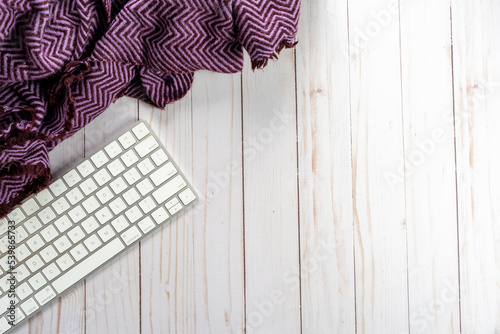 Computer keyboard with a purple blanket, on wood background. Top down, flat lay view with copyspace