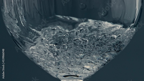 Closeup water pouring glass at dark background. Splashing fluid filling cup