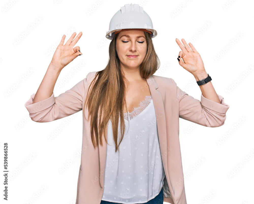 Young blonde woman wearing architect hardhat relax and smiling with eyes closed doing meditation gesture with fingers. yoga concept.