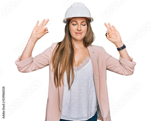 Young blonde woman wearing architect hardhat relax and smiling with eyes closed doing meditation gesture with fingers. yoga concept.