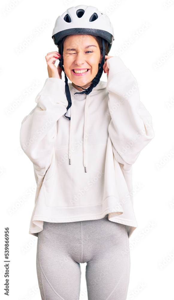 Beautiful brunette young woman wearing bike helmet and sporty clothes covering ears with fingers with annoyed expression for the noise of loud music. deaf concept. Beautiful brunette young woman wearing bike helmet and sporty clothes covering ears with fingers with annoyed expression for the noise of loud music. deaf concept.