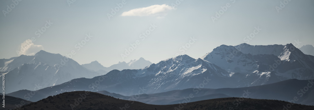 Monochrome panorama of the mountain snow-capped peaks of the Caucasus with snow and glaciers in side lighting, on a sunny summer morning
