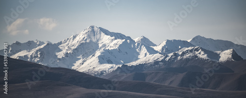 Panorama of the peaks of the high mountains of the Caucasus with snow and glaciers and hills with vegetation in the mountains in summer, tonal perspective on a summer sunny morning