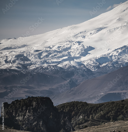 Mountain slope with glaciers and snow cover in the Caucasus close up with hills with vegetation, sunny summer morning