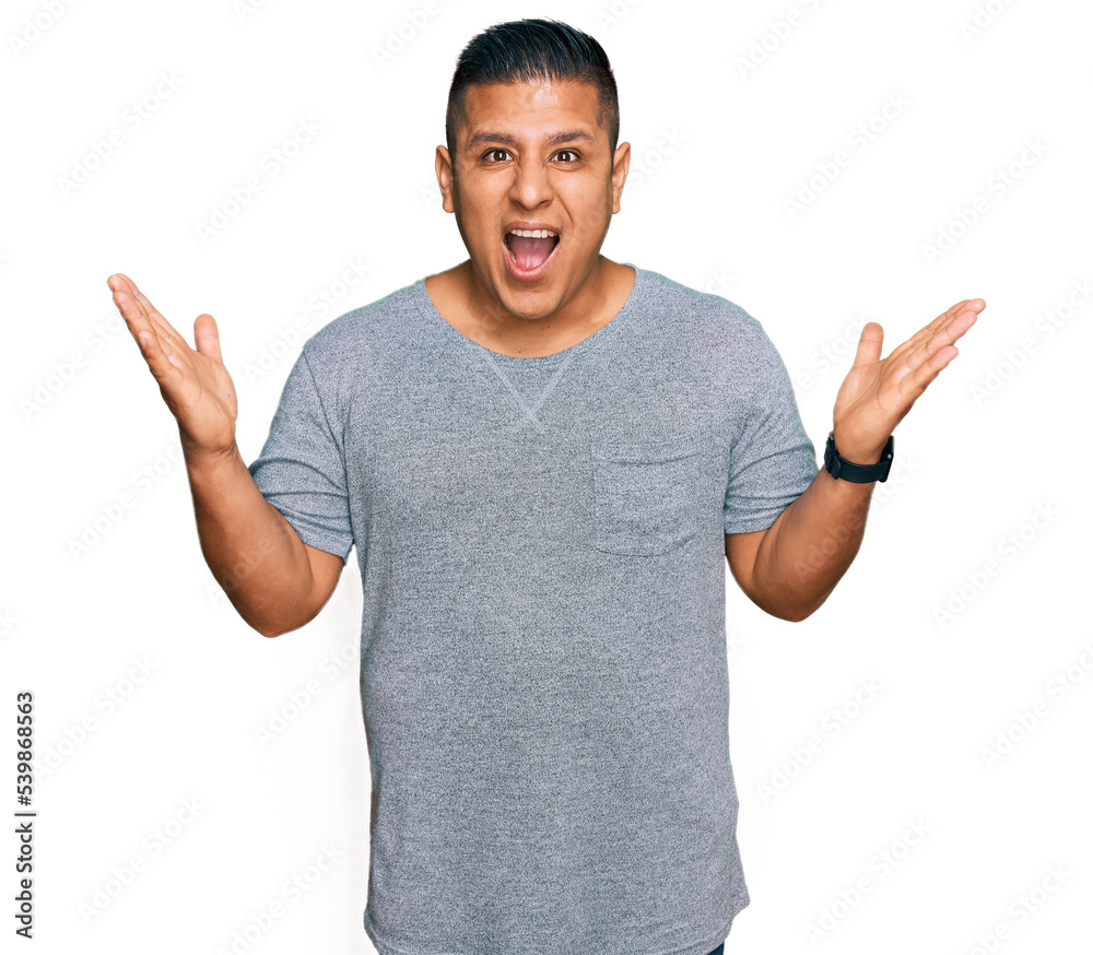 Fototapeta premium Young latin man wearing casual clothes celebrating crazy and amazed for success with arms raised and open eyes screaming excited. winner concept