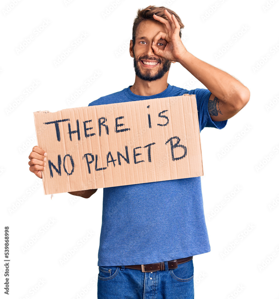 Handsome blond man with beard holding there is no planet b banner smiling happy doing ok sign with hand on eye looking through fingers Handsome blond man with beard holding there is no planet b banner smiling happy doing ok sign with hand on eye looking through fingers