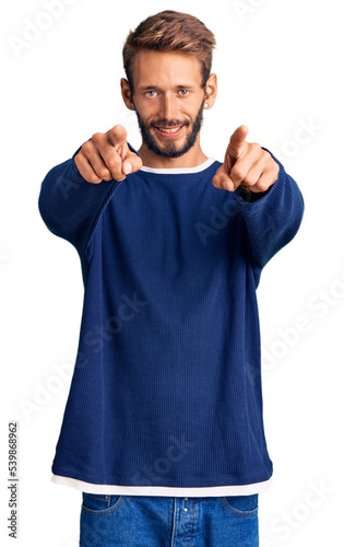 Handsome blond man with beard wearing casual sweater pointing to you and the camera with fingers, smiling positive and cheerful