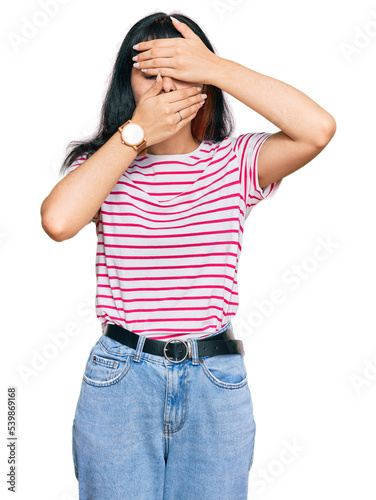 Young hispanic girl wearing casual clothes covering eyes and mouth with hands, surprised and shocked. hiding emotion