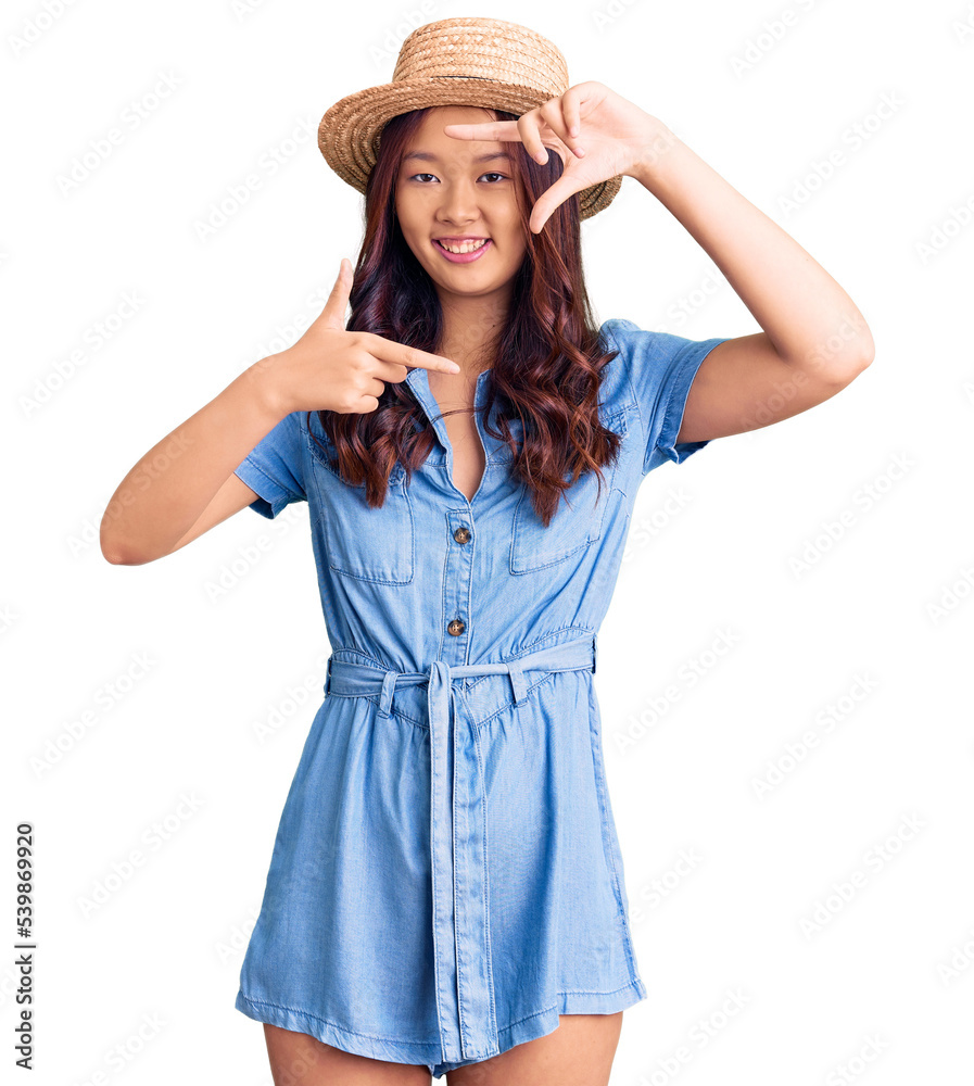 Young beautiful chinese girl wearing summer hat smiling making frame with hands and fingers with happy face. creativity and photography concept. Young beautiful chinese girl wearing summer hat smiling making frame with hands and fingers with happy face. creativity and photography concept.