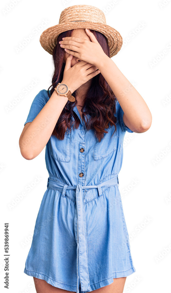 Young beautiful chinese girl wearing summer hat covering eyes and mouth with hands, surprised and shocked. hiding emotion Young beautiful chinese girl wearing summer hat covering eyes and mouth with hands, surprised and shocked. hiding emotion