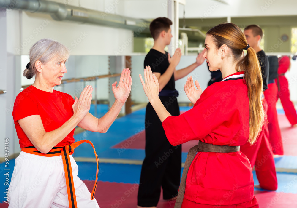 Senior and younger women sparring during group karate training.