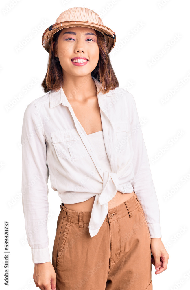 Young beautiful chinese girl wearing explorer hat looking positive and happy standing and smiling with a confident smile showing teeth Young beautiful chinese girl wearing explorer hat looking positive and happy standing and smiling with a confident smile showing teeth