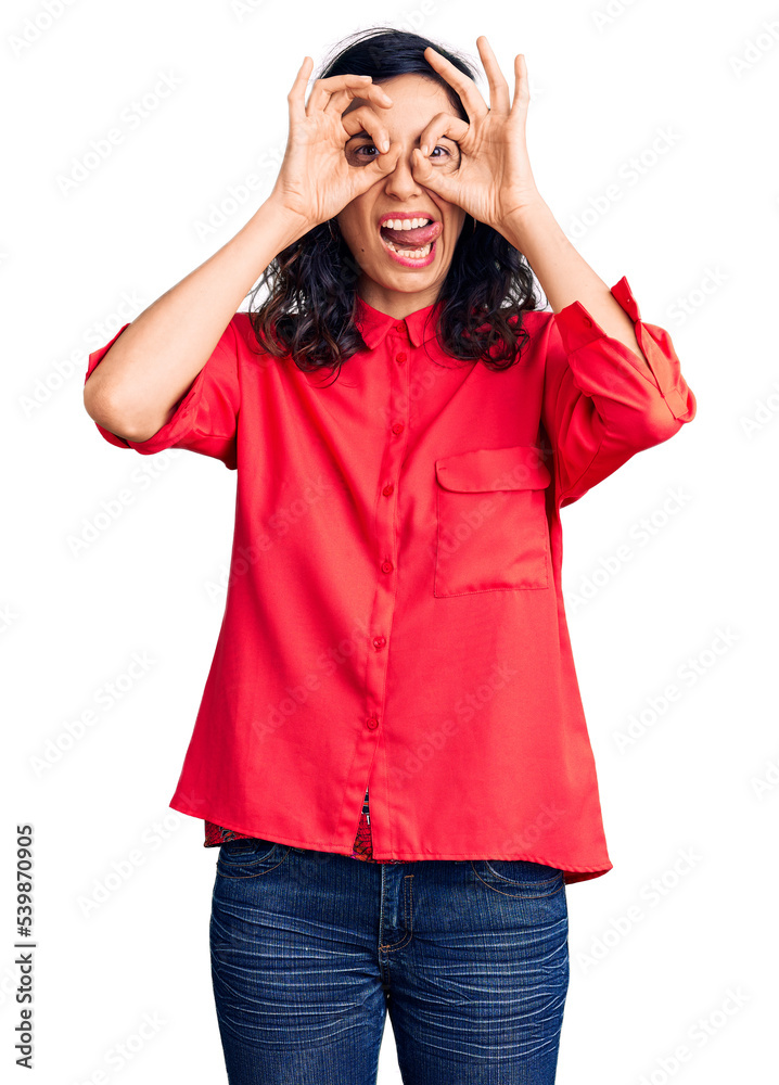 Young beautiful hispanic woman wearing casual clothes doing ok gesture like binoculars sticking tongue out, eyes looking through fingers. crazy expression. Young beautiful hispanic woman wearing casual clothes doing ok gesture like binoculars sticking tongue out, eyes looking through fingers. crazy expression.
