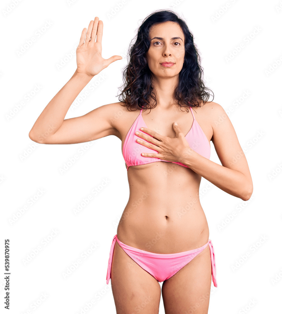 Fototapeta premium Young beautiful hispanic woman wearing bikini swearing with hand on chest and open palm, making a loyalty promise oath