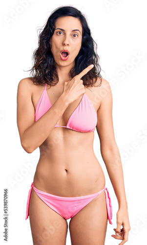 Young beautiful hispanic woman wearing bikini surprised pointing with finger to the side, open mouth amazed expression. © Krakenimages.com