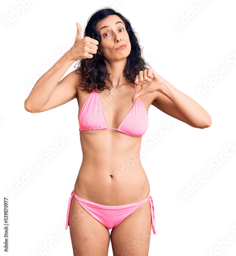 Young beautiful hispanic woman wearing bikini doing thumbs up and down, disagreement and agreement expression. crazy conflict