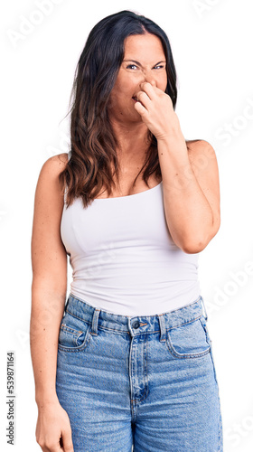 Young beautiful brunette woman wearing casual sleeveless t-shirt smelling something stinky and disgusting, intolerable smell, holding breath with fingers on nose. bad smell