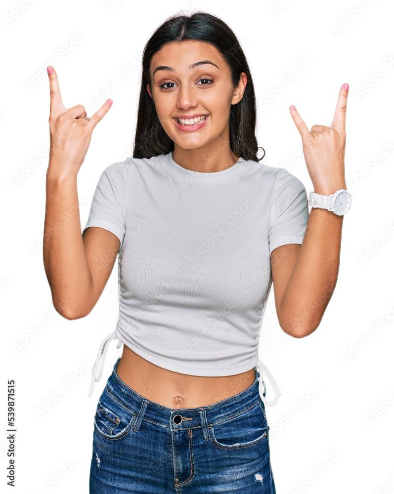 Young hispanic girl wearing casual white t shirt shouting with crazy expression doing rock symbol with hands up. music star. heavy music concept. Young hispanic girl wearing casual white t shirt shouting with crazy expression doing rock symbol with hands up. music star. heavy music concept.