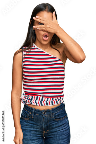 Beautiful hispanic woman wearing casual clothes peeking in shock covering face and eyes with hand, looking through fingers with embarrassed expression.