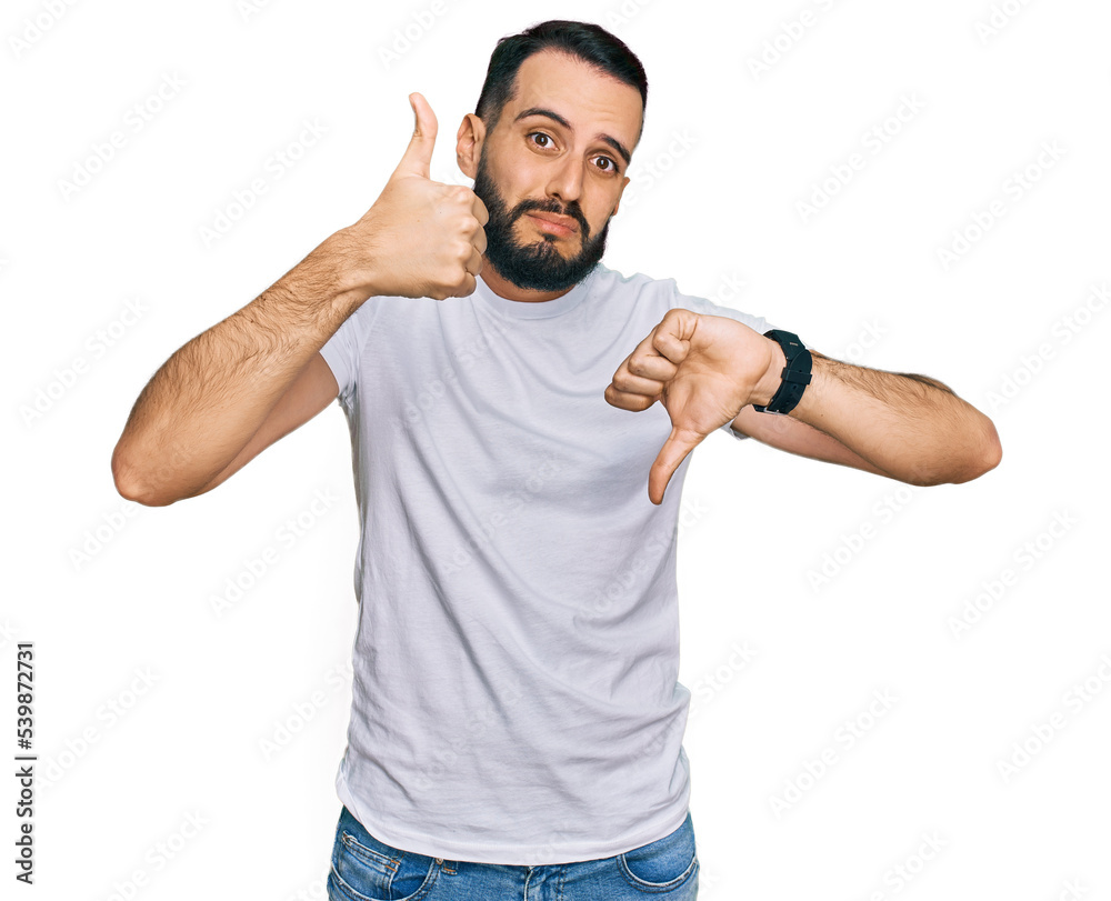 Young man with beard wearing casual white t shirt doing thumbs up and down, disagreement and agreement expression. crazy conflict Young man with beard wearing casual white t shirt doing thumbs up and down, disagreement and agreement expression. crazy conflict