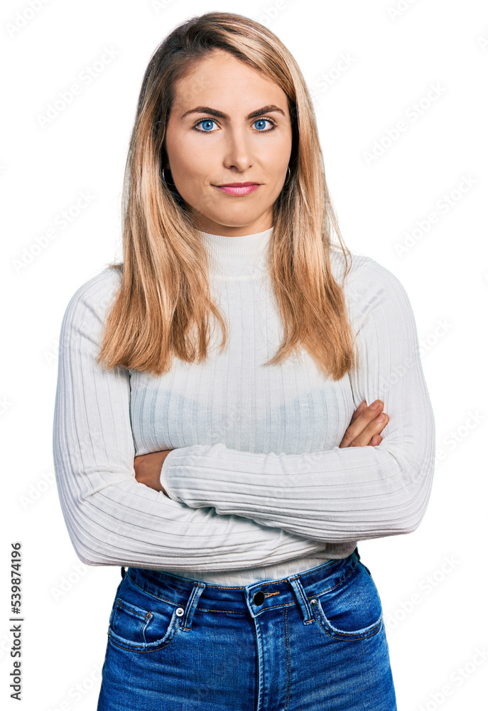 Young blonde woman with arms crossed gesture relaxed with serious expression on face. simple and natural looking at the camera.