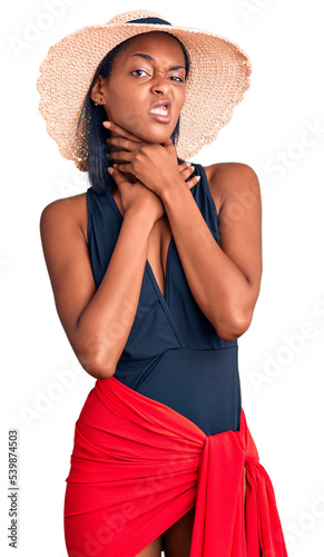 Young african american woman wearing swimsuit and summer hat shouting suffocate because painful strangle. health problem. asphyxiate and suicide concept.