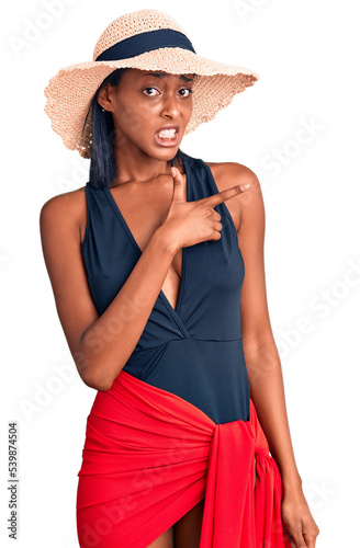 Young african american woman wearing swimsuit and summer hat pointing aside worried and nervous with forefinger, concerned and surprised expression