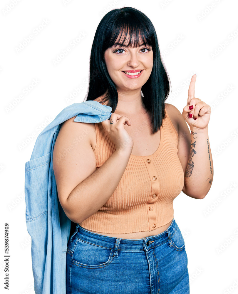 Young hispanic plus size woman wearing holding denim jacket smiling with an idea or question pointing finger with happy face, number one Young hispanic plus size woman wearing holding denim jacket smiling with an idea or question pointing finger with happy face, number one