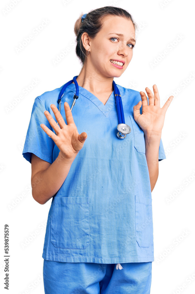 Young beautiful blonde woman wearing doctor uniform and stethoscope disgusted expression, displeased and fearful doing disgust face because aversion reaction. with hands raised Young beautiful blonde woman wearing doctor uniform and stethoscope disgusted expression, displeased and fearful doing disgust face because aversion reaction. with hands raised