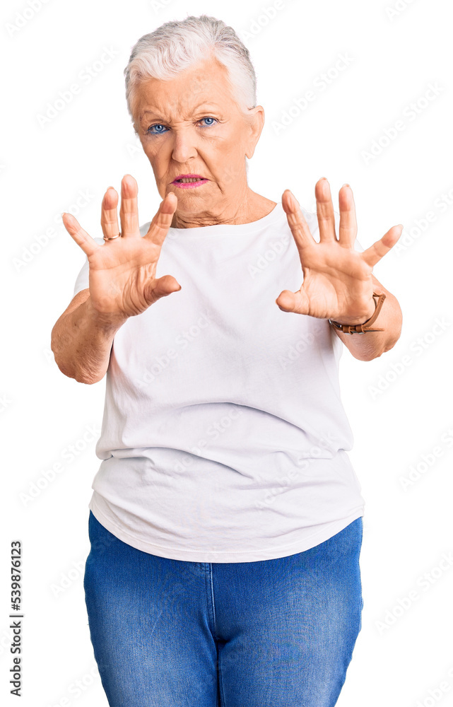 Senior beautiful woman with blue eyes and grey hair wearing casual white tshirt afraid and terrified with fear expression stop gesture with hands, shouting in shock. panic concept. Senior beautiful woman with blue eyes and grey hair wearing casual white tshirt afraid and terrified with fear expression stop gesture with hands, shouting in shock. panic concept.