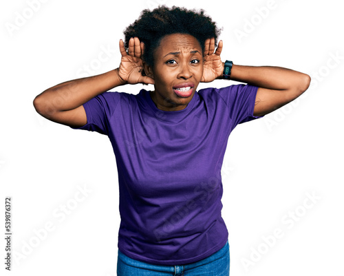African american woman with afro hair wearing casual purple t shirt trying to hear both hands on ear gesture, curious for gossip. hearing problem, deaf