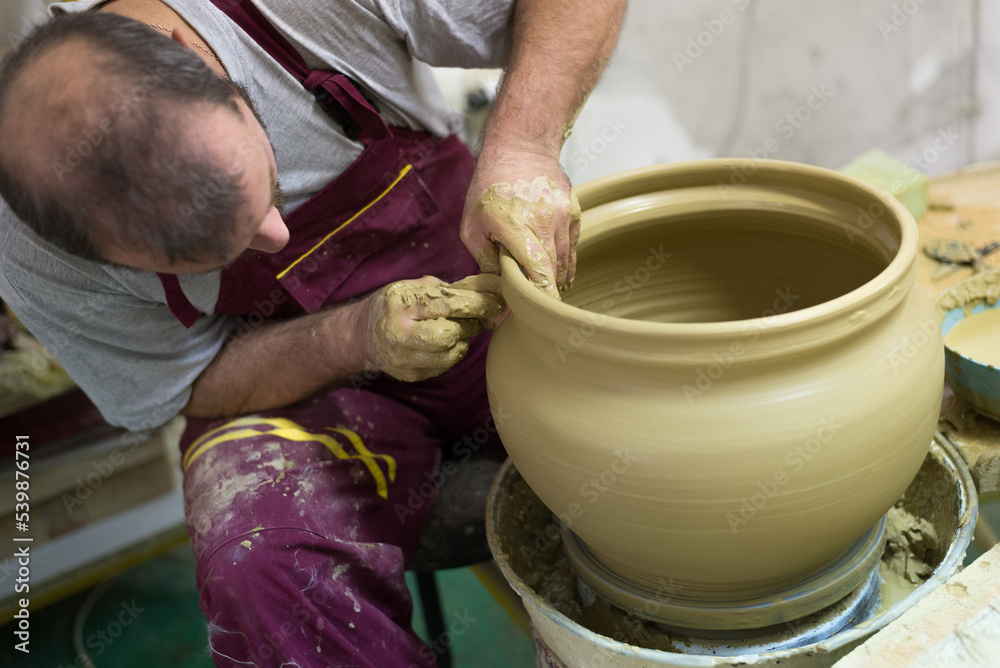 Man professional potter making pottery from wet clay in his pottery workshop